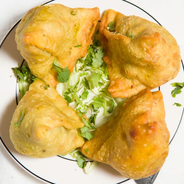 Four golden-brown samosas, garnished with fresh cilantro and shredded lettuce, on a white plate.