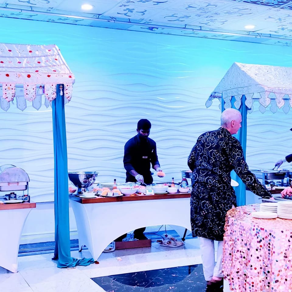 A Guru Palace buffet with a server and guests, featuring Indian dishes under decorative canopies.