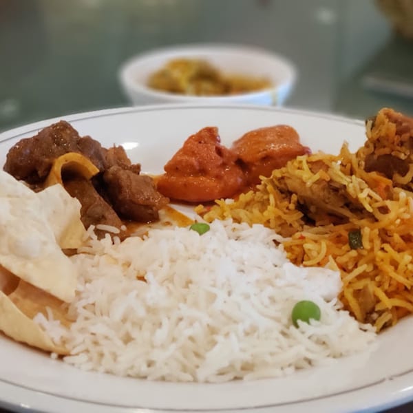 A Guru Palace Indian dish with white rice, biryani, chicken tikka masala, and lamb curry.