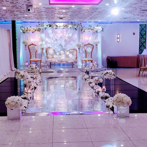An elegant wedding stage with white and gold seating, floral arrangements, and a reflective walkway.
