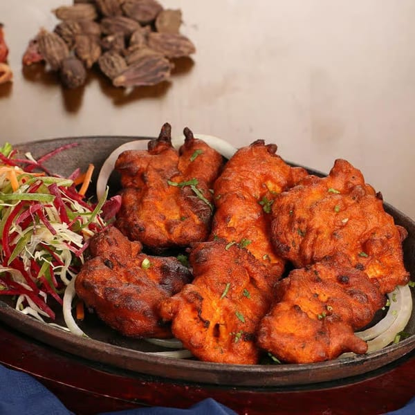 Guru Palace's Indian chicken pakora, garnished with fresh herbs, onions, and a side salad.
