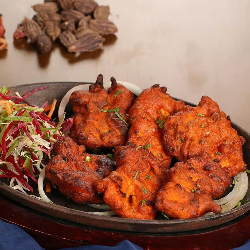 Guru Palace's Indian chicken pakora, garnished with fresh herbs, onions, and a side salad.