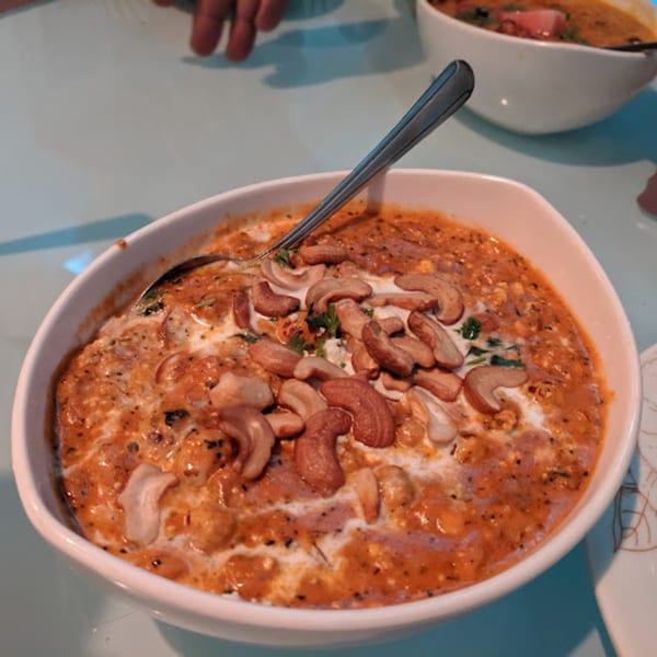 A white bowl of Indian curry with cashews and cream, with a spoon resting in it.