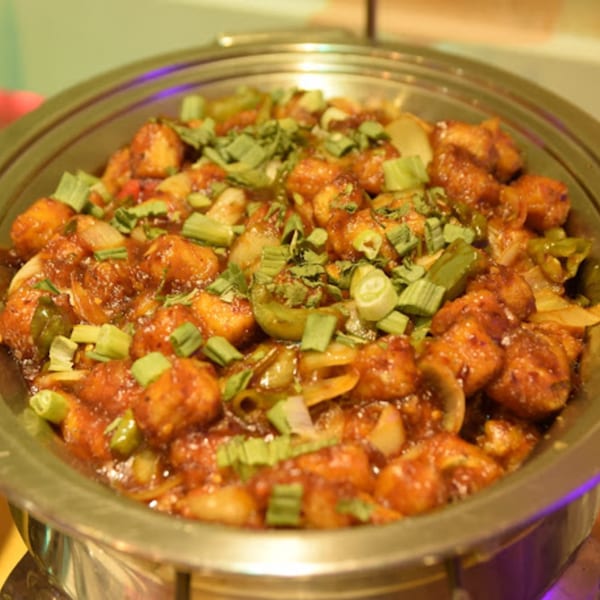 Close-up of a large metal serving dish filled with Guru Palace's chili paneer, garnished with green onions.