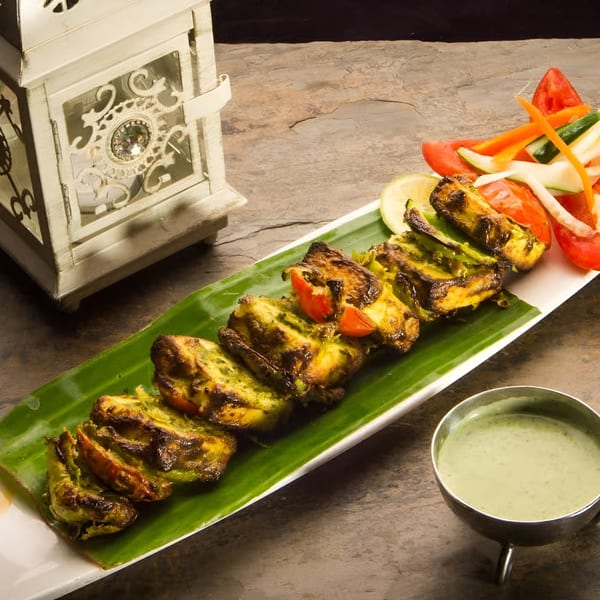 Grilled Indian paneer tikka with vegetables and green chutney, next to a decorative lantern.