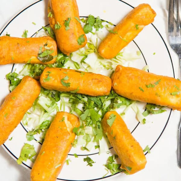 Eight golden-brown paneer pakora pieces, garnished with cilantro, arranged on a bed of shredded lettuce.