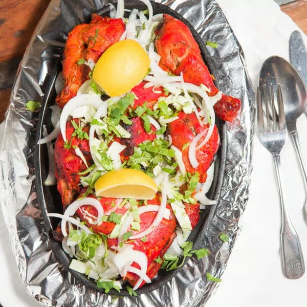 Guru Palace's Tandoori Chicken, garnished with onions, cilantro, and lemon wedges, served on foil.