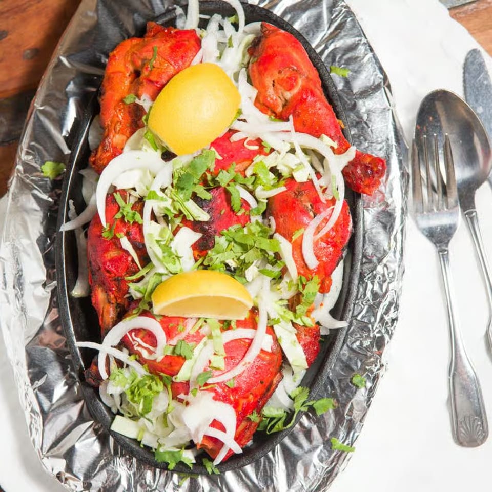 Guru Palace's Tandoori Chicken, garnished with onions, cilantro, and lemon wedges, served on foil.