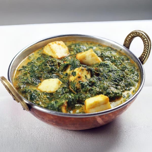 Guru Palace's Palak Paneer, a vibrant green spinach curry with cubes of paneer cheese in a copper karahi.