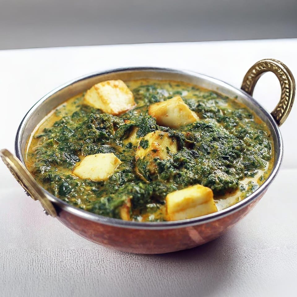 Guru Palace's Palak Paneer, a vibrant green spinach curry with cubes of paneer cheese in a copper karahi.