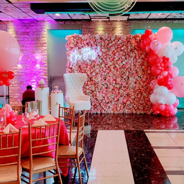 A Guru Palace event space with pink floral wall, "Oh Baby" neon sign, balloons, and red-draped tables.