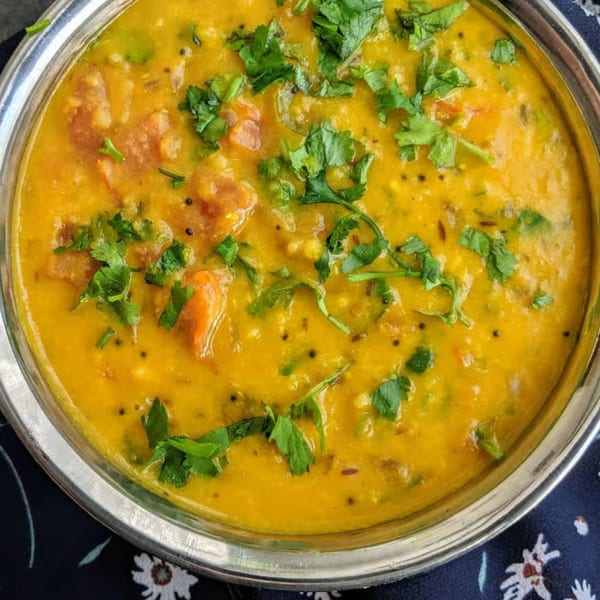 Close-up of a vibrant yellow Indian dal dish, garnished with fresh green cilantro in a silver bowl.